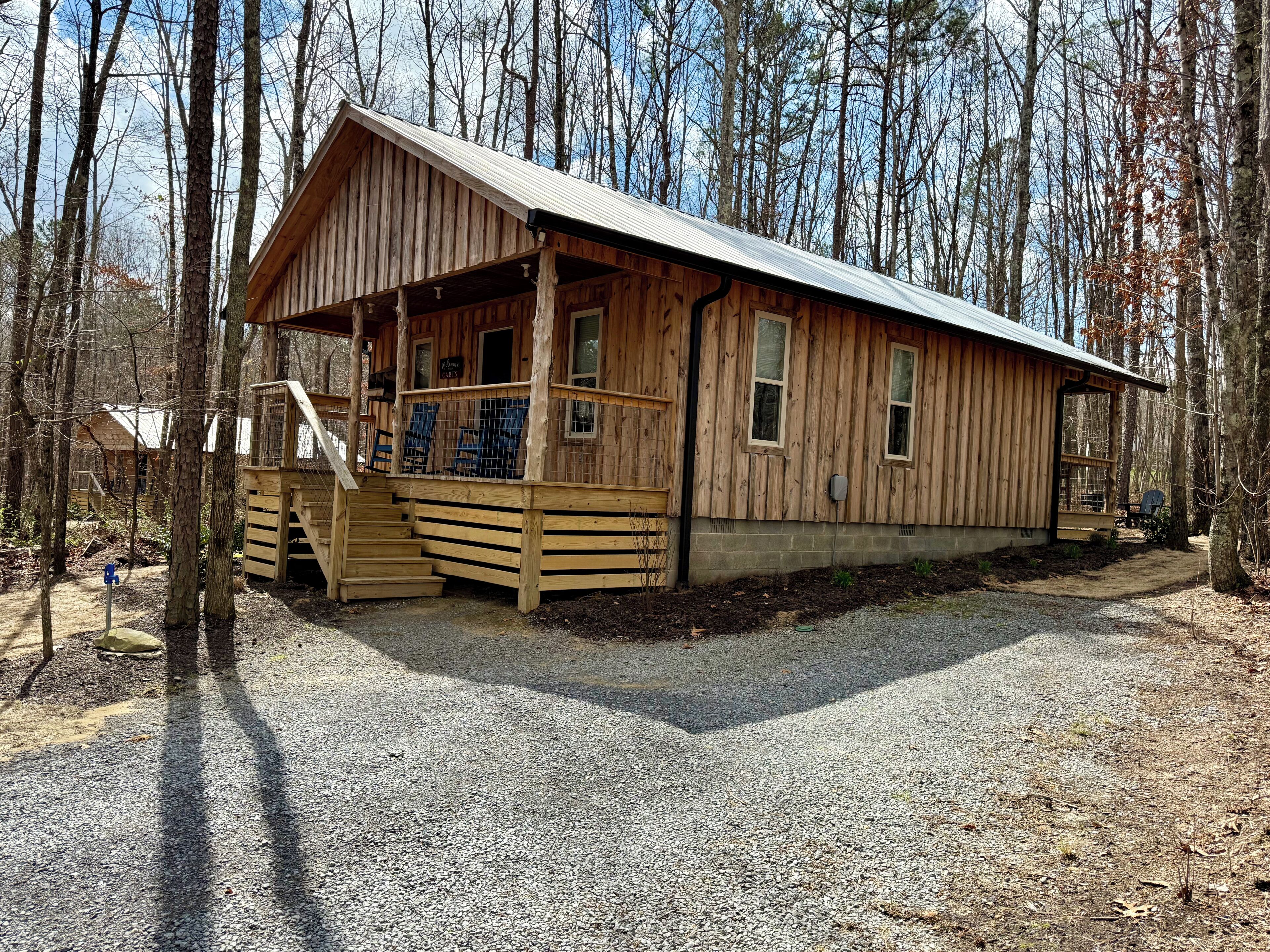 A wooden cabin with a porch, a staircase, and a gravel driveway.