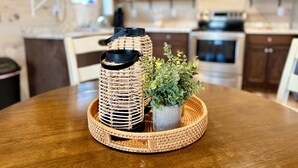 A round wooden table with a woven tray holding two wicker lanterns and a potted plant. - Squirrel's Nest (Fort Payne)