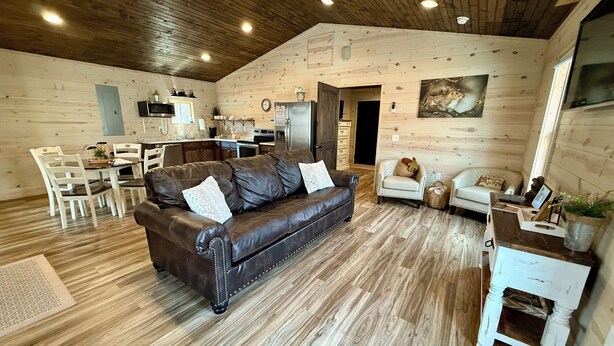 A cozy living room with a leather sofa, wooden flooring, and a kitchen in the background. - Squirrel's Nest (Fort Payne)