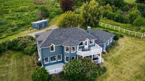A large, two-story house with a balcony, surrounded by a well-maintained lawn and a forested hill in the background. - Benchwarmer`s Bliss (Homer)