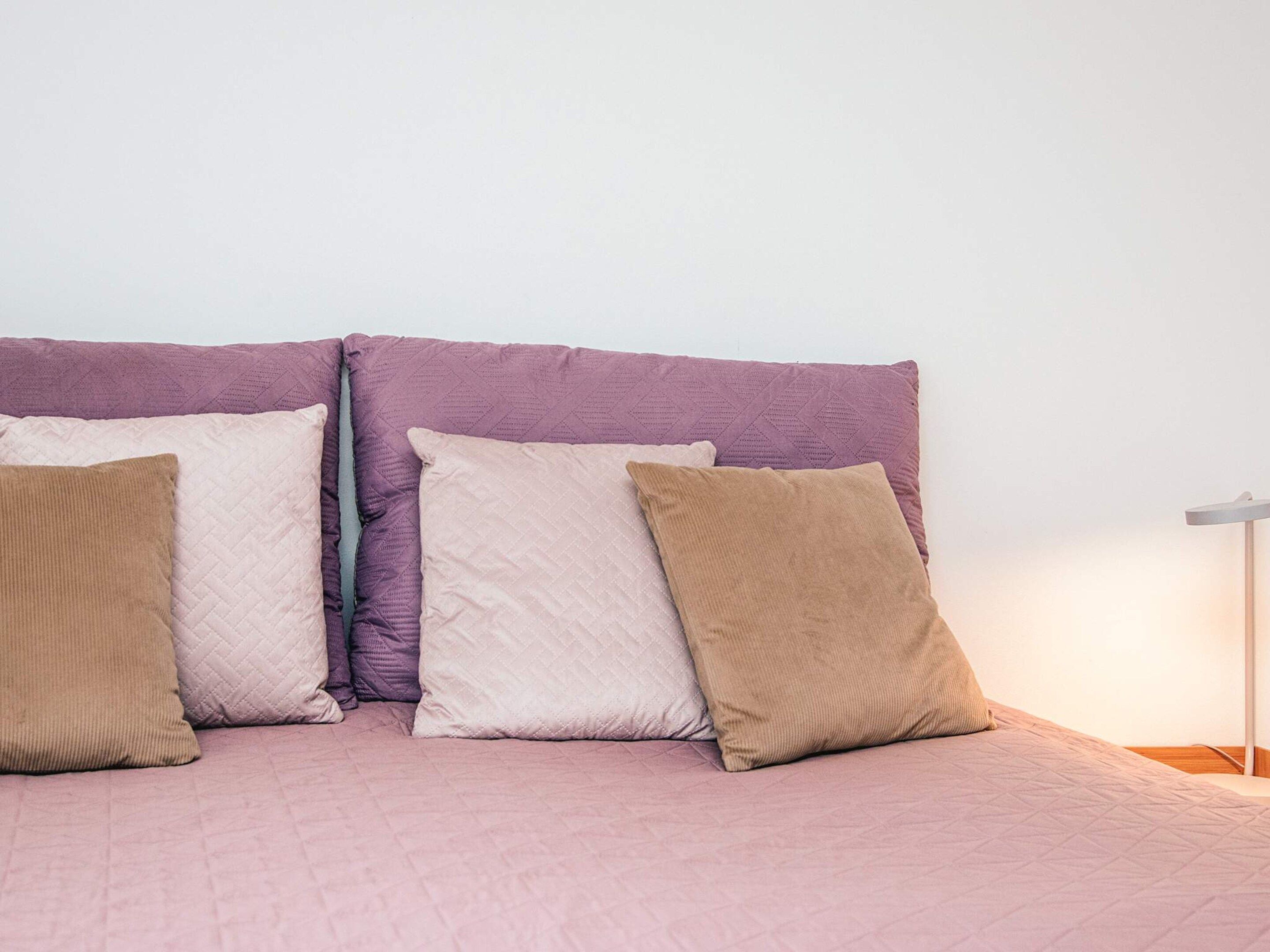 A bed with a headboard and four pillows in different colors.