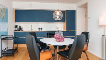 A modern kitchen with blue cabinets, a round dining table with black chairs, and a hanging pendant light.