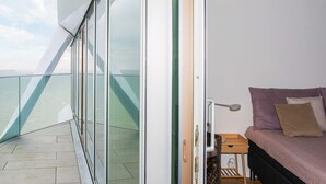 A balcony with a glass railing, a bed with pillows, a small wooden table, and a view of the sea. - 5 Star Holiday Home in Aarhus C (Aarhus)