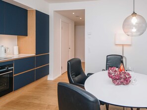 Une cuisine moderne avec des meubles de couleur bleu foncé, un plan de travail blanc et une table de salle à manger ronde, assortie de chaises.