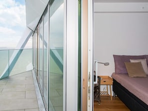 A balcony with a glass railing, a bed with pillows, and a small wooden table. - 5 Star Holiday Home in Aarhus C (Aarhus)