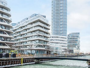 Un ensemble immobilier moderne composé de plusieurs étages, doté de grandes fenêtres et surmonté d’un pont qui enjambe une étendue d’eau.