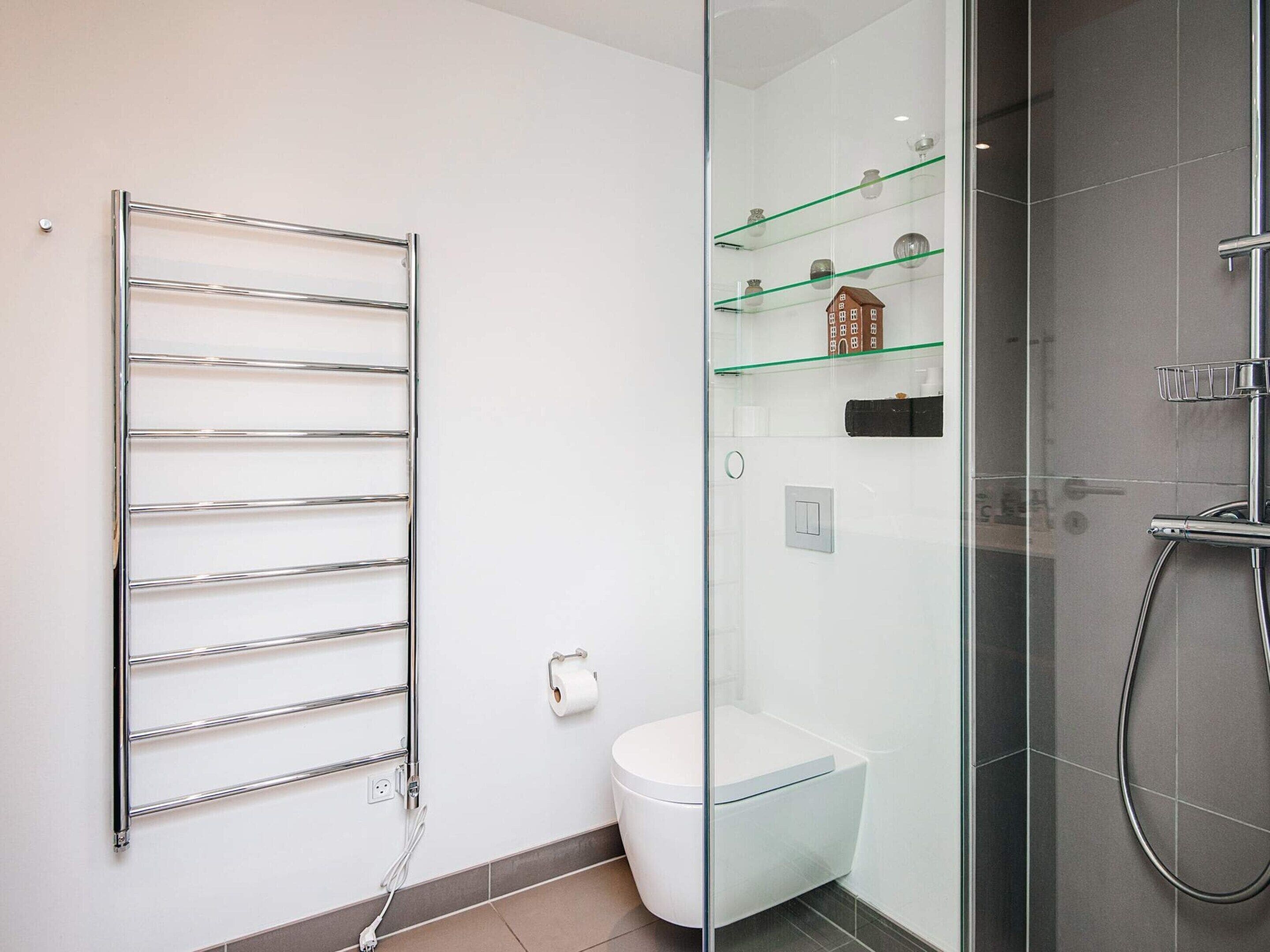 A modern bathroom with a glass shower enclosure, a chrome towel rack, and a toilet.