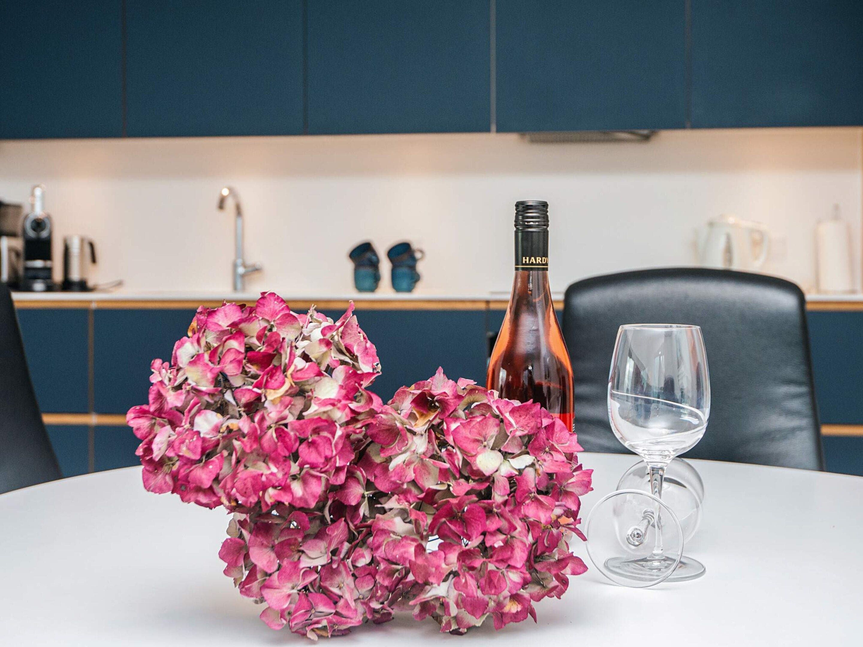 A table with a bottle of wine, a glass, and a bouquet of pink flowers.