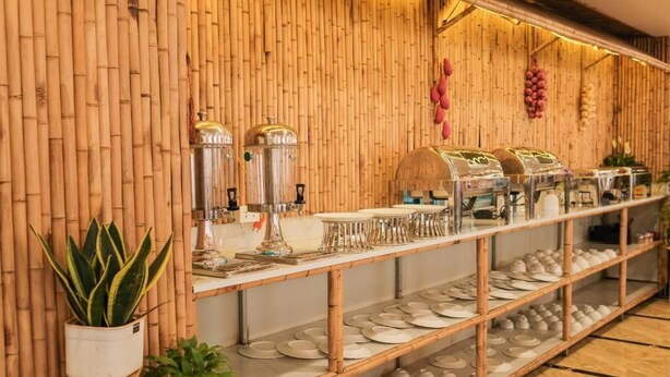 A buffet area with bamboo walls, a variety of dishes, and a selection of plates and bowls on shelves. - Flamant Boutique Hotel (Sa Pa)