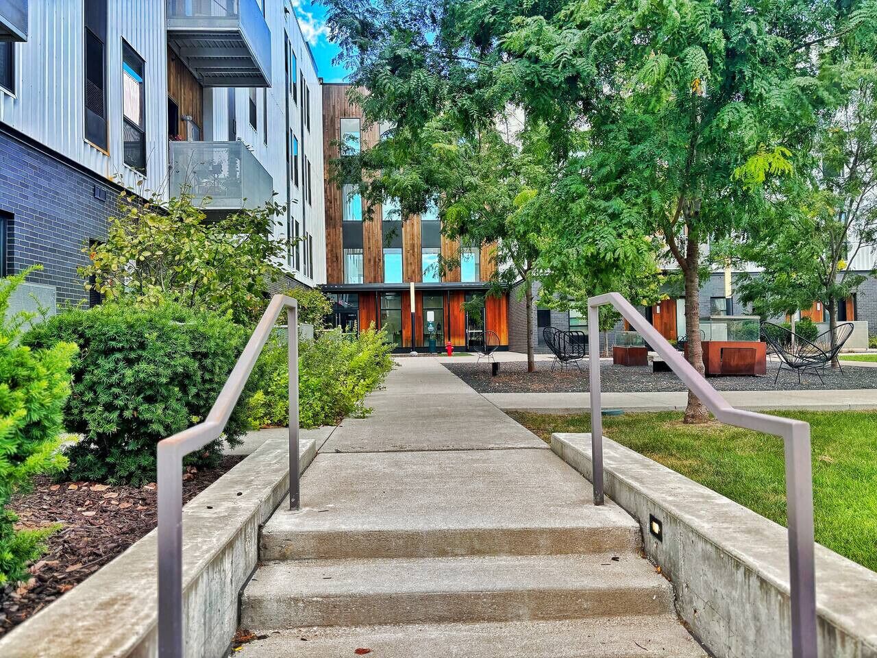 A concrete staircase leading to a building with a modern design, surrounded by greenery and outdoor seating areas.