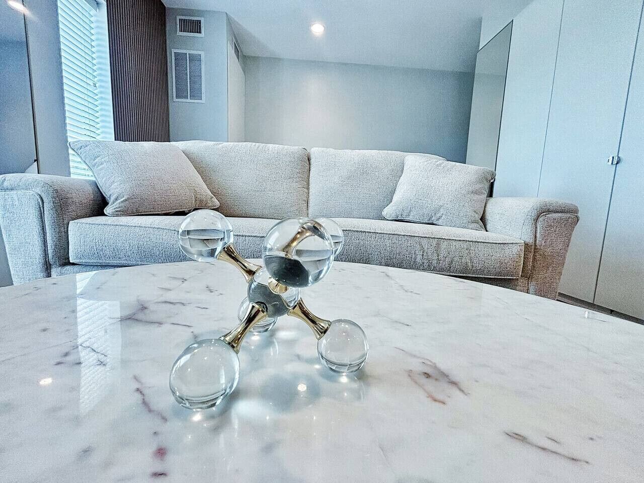 A modern living room with a marble coffee table, a grey sofa, and a large mirror.