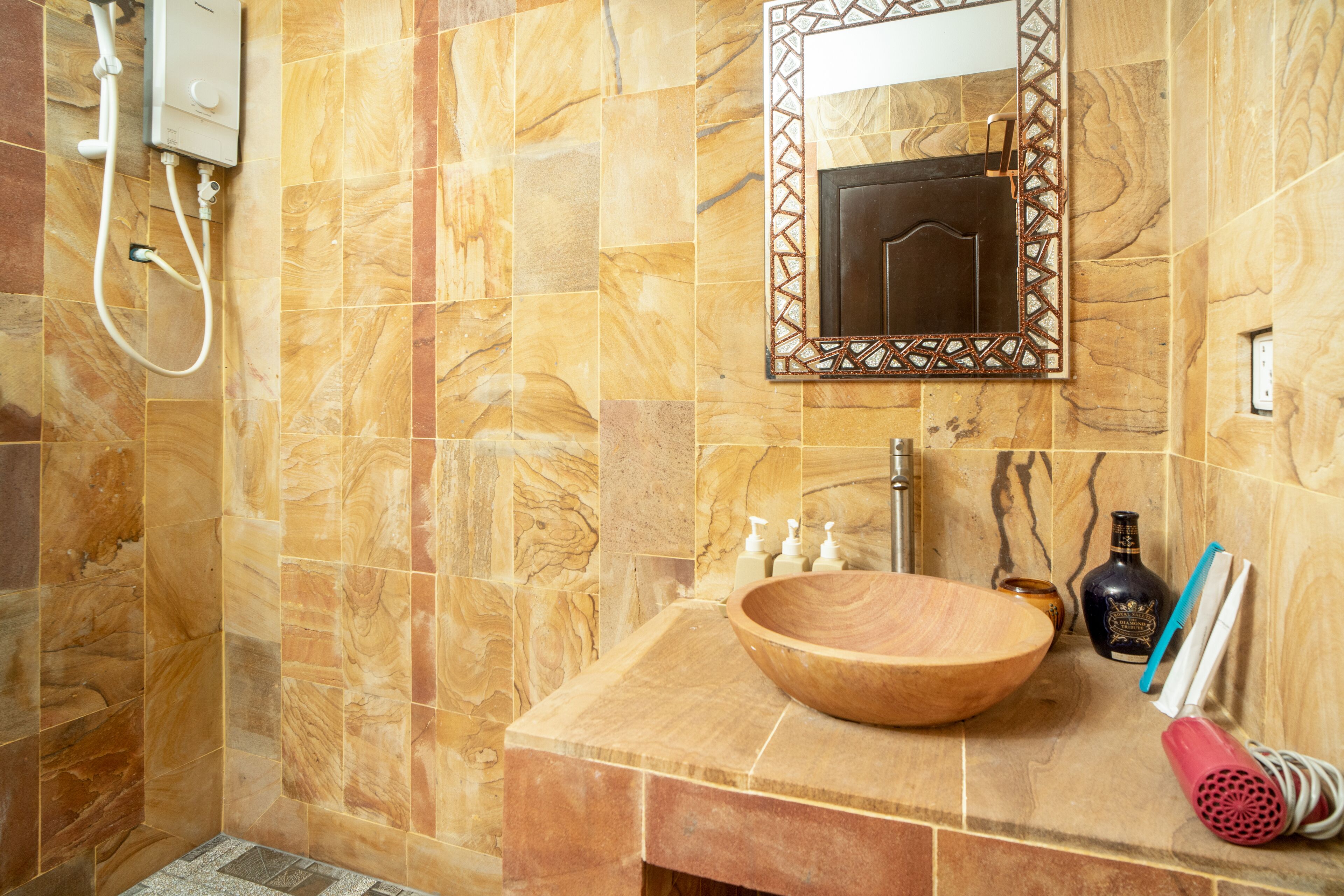 A bathroom with a wooden sink, a mirror with a decorative frame, a handheld showerhead, and toiletries.