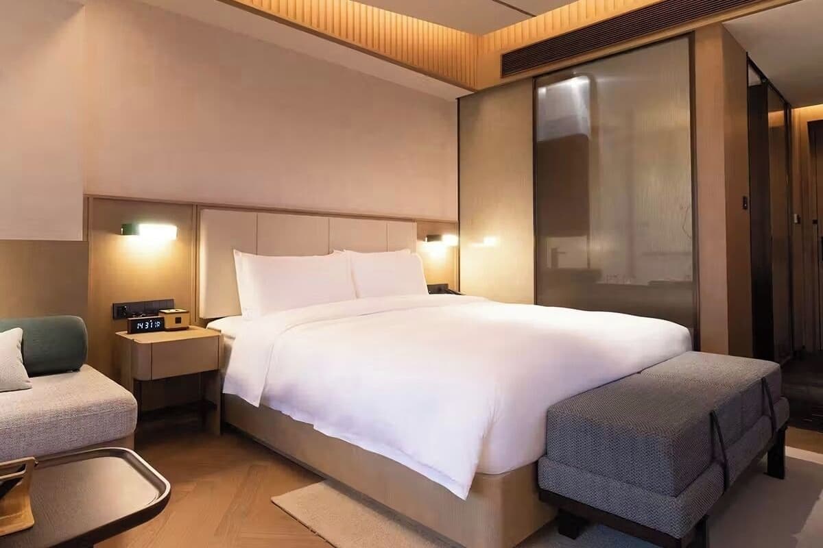 A modern hotel room with a large bed, bedside tables, a desk, and a seating area.
