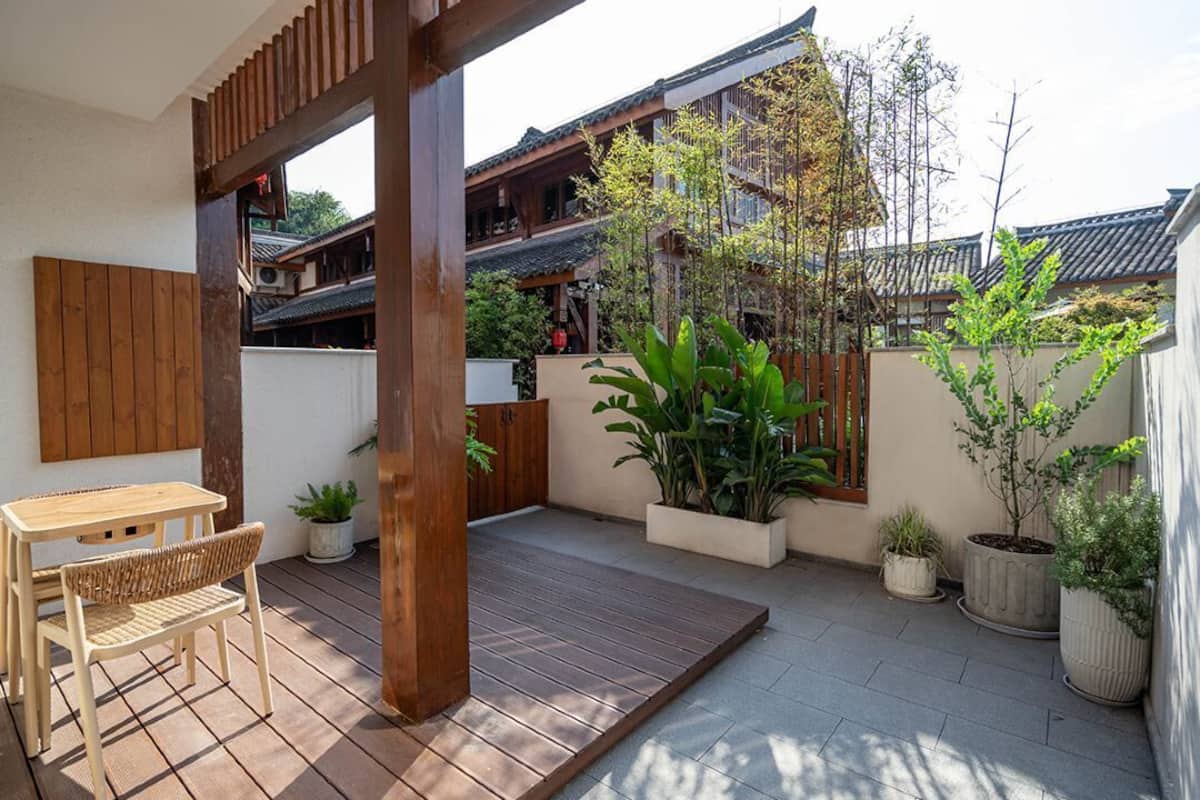 A traditional Japanese-style outdoor space with a wooden table and bench, potted plants, and a view of traditional buildings in the background.