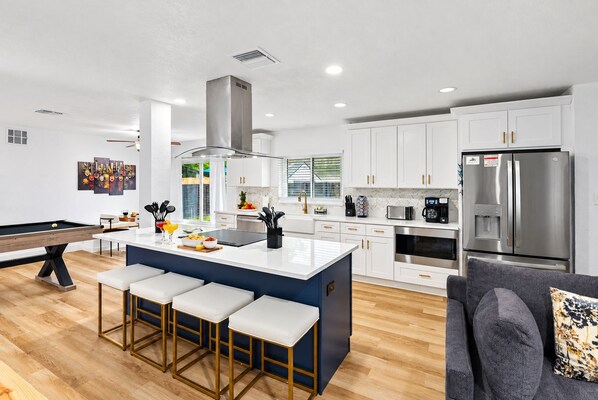 A modern kitchen with white cabinets, a central island with bar stools, a built-in microwave, and a stainless steel refrigerator.