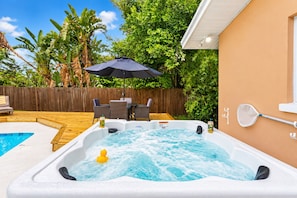 Ein Whirlpool mit Holzterrasse, einem Tisch mit Stühlen und einem Pool im Hintergrund.