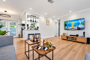 Una sala de estar moderna con una mesa de centro de madera, consolas de videojuegos, un televisor de pantalla plana y una zona de estar acogedora.
