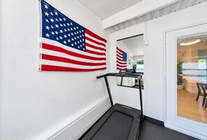 Un couloir avec un tapis de course, une porte donnant sur une pièce et deux drapeaux américains accrochés au mur.