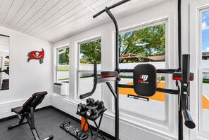 Une salle de sport équipée de matériel d’exercice, d’un banc et d’un porte-haltères fixé au mur.