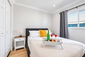 A hotel room with a bed, bedside table, nightstand, and a window with curtains.