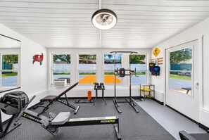 Un gimnasio con equipo de ejercicio, una cinta de correr y vistas a una cancha de tenis.