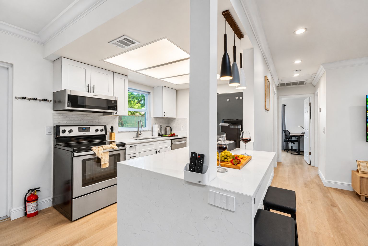 A modern kitchen with stainless steel appliances, a central island, pendant lighting, and a view of the outdoors.
