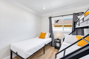 A compact room with two single beds, a small table, a lamp, and a window with curtains.