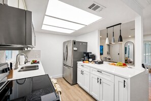 Une cuisine moderne équipée d’un réfrigérateur en acier inoxydable, d’une machine à café et d’un panier à fruits posé sur le plan de travail.
