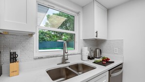 Eine moderne Küche mit weißen Schränken, einer doppelten Spüle und einem Fenster mit Blick ins Grüne.