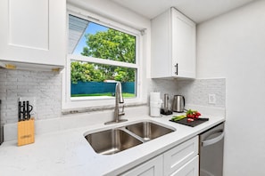 Une cuisine moderne dotée d’un évier à deux bacs, de meubles blancs et d’une fenêtre donnant sur un jardin verdoyant.