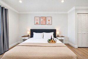 A hotel room with a large bed, two bedside tables, a tray with fruits and drinks, and a closet with sliding doors.
