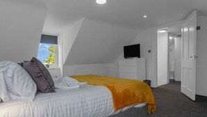 Een moderne slaapkamer met een bed, een televisie en een raam met uitzicht op groen.