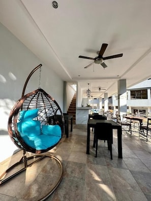 A spacious living area with a hanging chair, a dining table, and a ceiling fan. - Harbour Bliss Hotel (Coron)