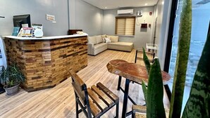 A modern reception area with a wooden reception desk, a sofa, and a dining table. - Harbour Bliss Hotel (Coron)