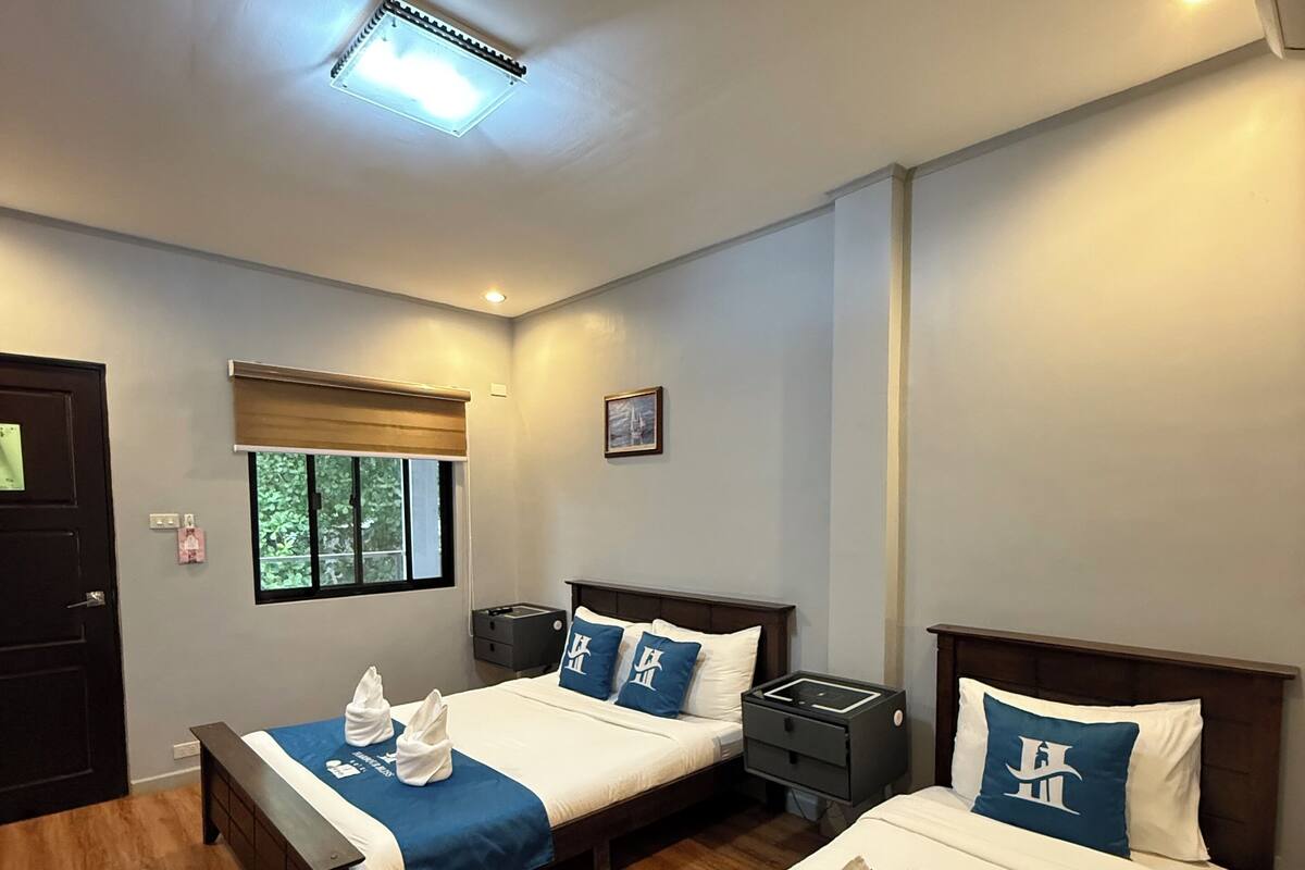 A hotel room with two beds, each with a blue and white bedspread, a wooden headboard, and a small bedside table with a lamp.
