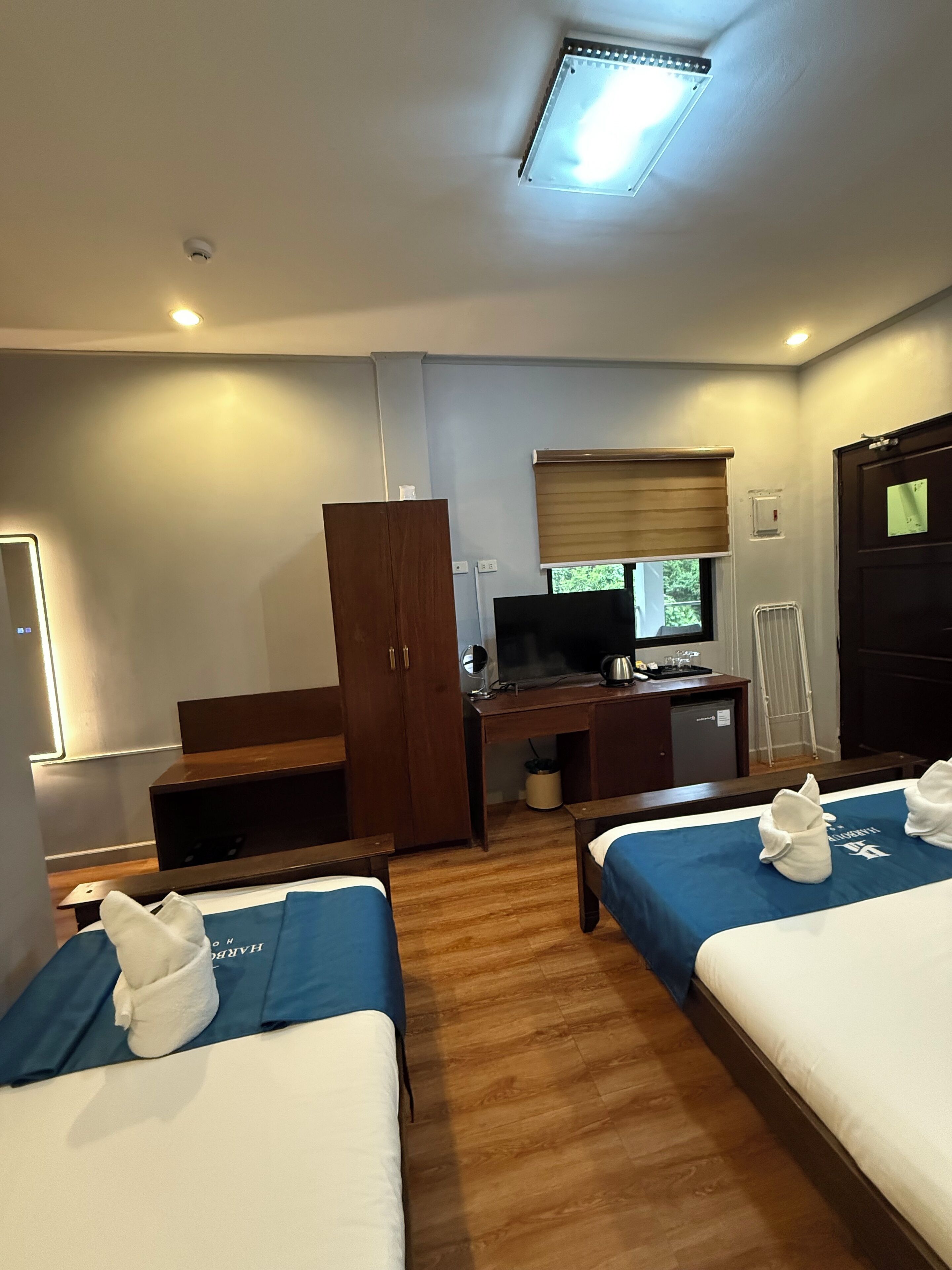A hotel room with two beds, a desk, a wardrobe, a television, and a window with blinds.