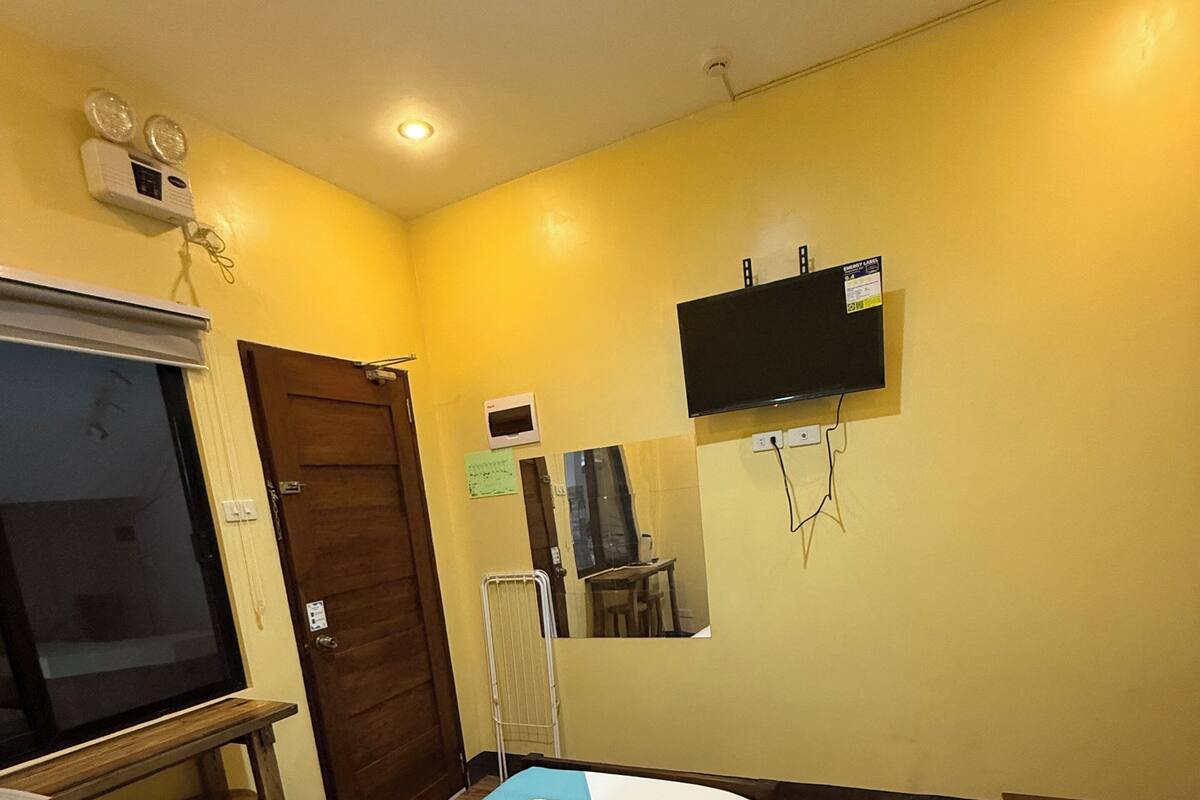 A hotel room with two beds, a TV mounted on the wall, a wooden floor, and a window with blinds.