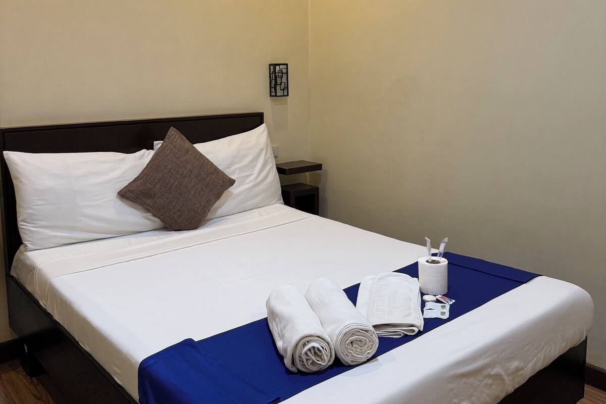 A neatly made bed with white linens, a blue accent, and rolled towels.