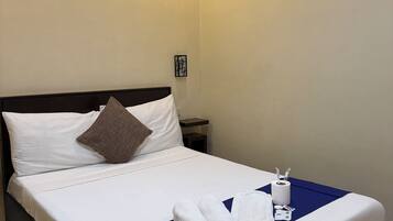 Una cama bien tendida con sábanas blancas, un detalle en azul y toallas enrolladas.