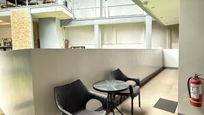 A dining area with wicker chairs and a glass table, a fire extinguisher mounted on the wall, and a view of the upper floor with a balcony. - Harbour Bliss Hotel (Coron)