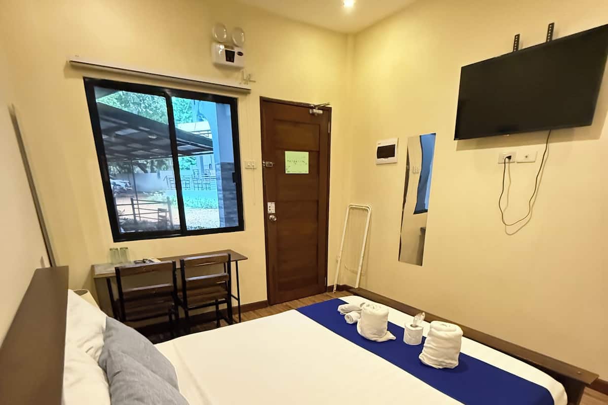 A hotel room with a bed, a desk, a chair, a window, a door, and a TV mounted on the wall.