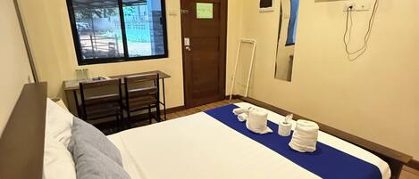 Habitación de hotel con cama, escritorio, silla, ventana, puerta y televisor montado en la pared.