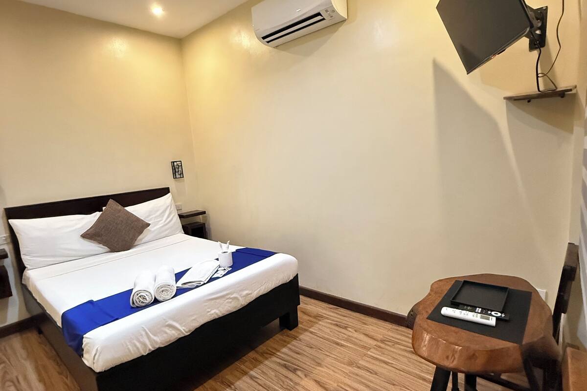 A hotel room with a bed, bedside table, and a small wooden chair.