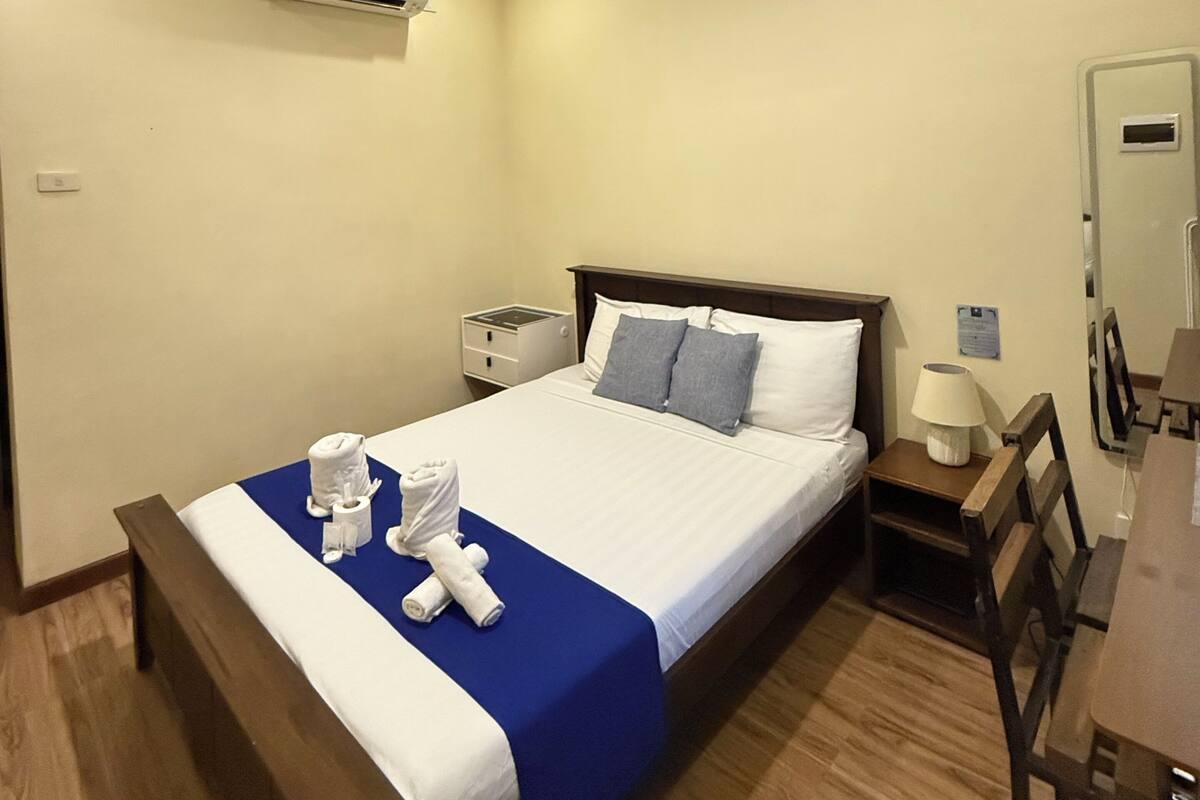 A hotel room with a bed, bedside tables, an air conditioning unit, a desk, and a chair.
