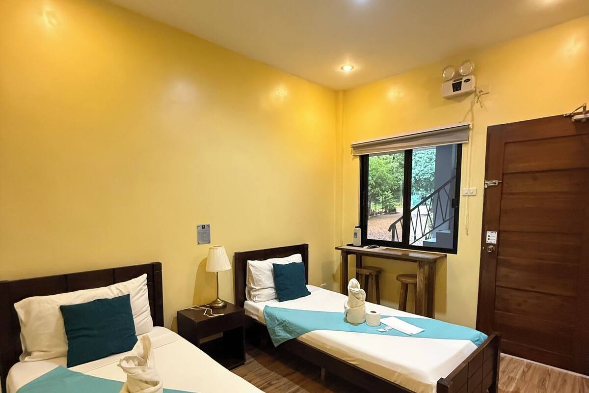 A hotel room with two beds, a desk, a window, and a door.
