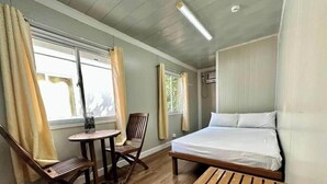 A room with a bed, a small table, a chair, and two windows with curtains. - Harbour Bliss Hotel (Coron)