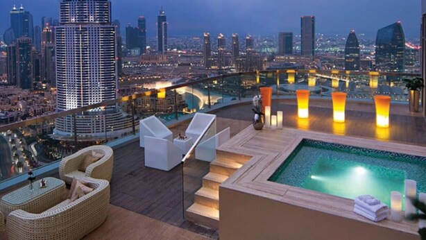 A rooftop terrace with a pool, lounge chairs, and a city view.