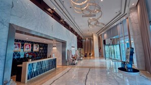 A spacious lobby with a reception desk, seating area, and a modern chandelier.