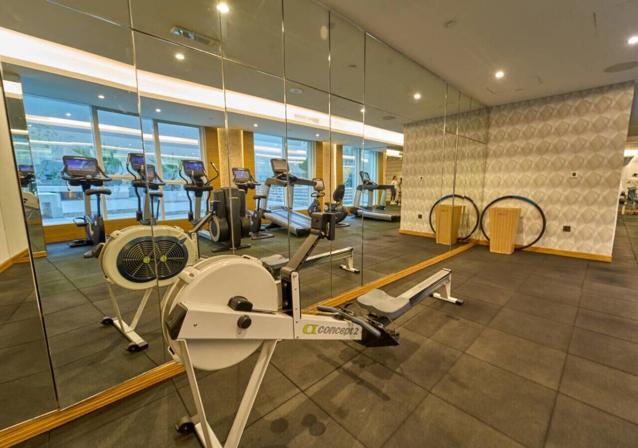 Un gimnasio con máquinas de cardio, una máquina de remo y un espejo que refleja el equipo.