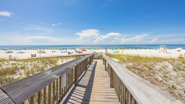 Een houten looppad dat naar een strand leidt, met parasols en strandstoelen.